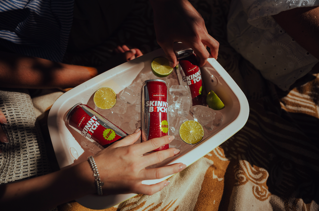 Three SKINNY B!TCH cans on ice in a cooler with lime halves